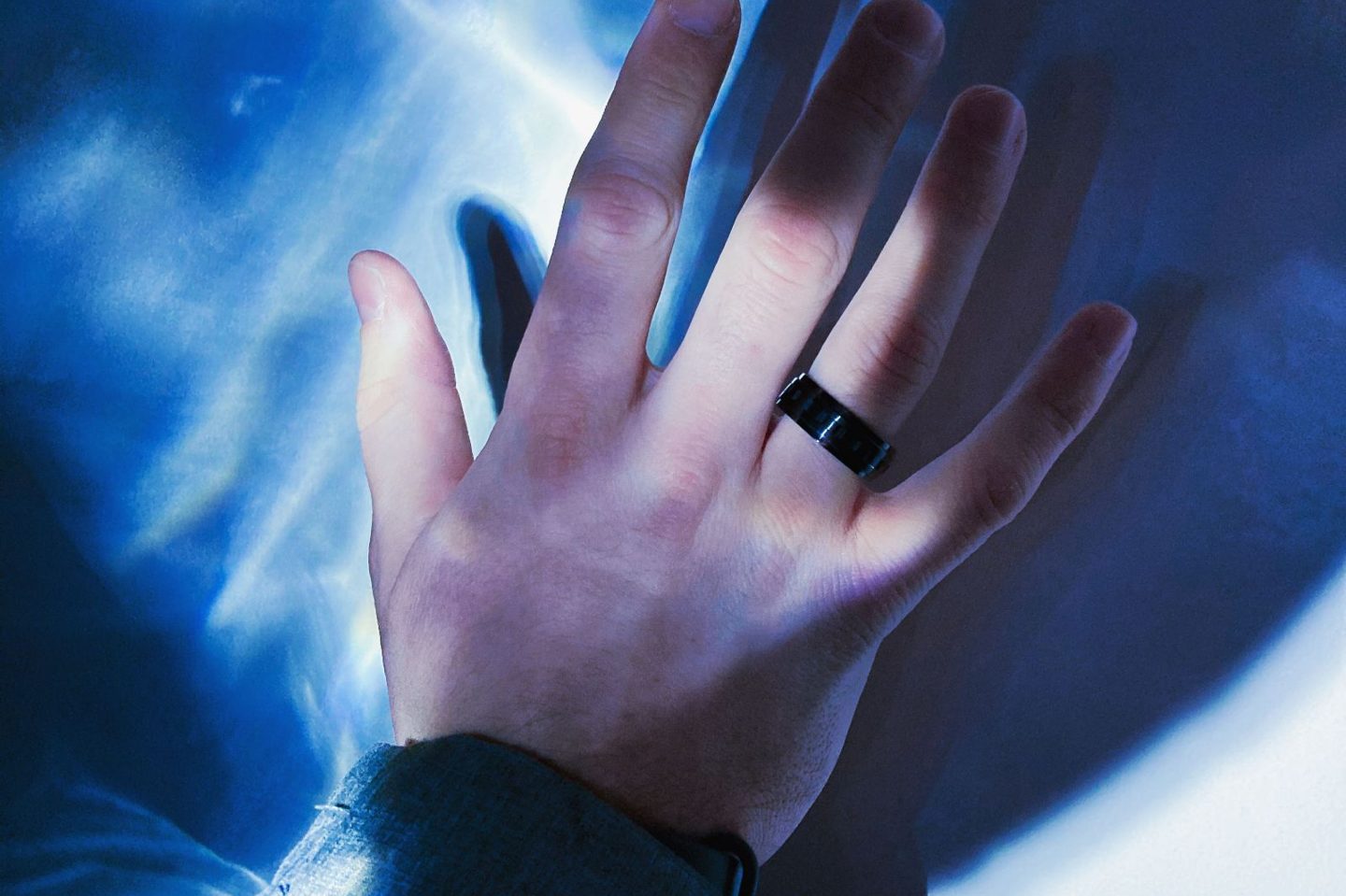 A hand wearing a smart ring in cool blue light