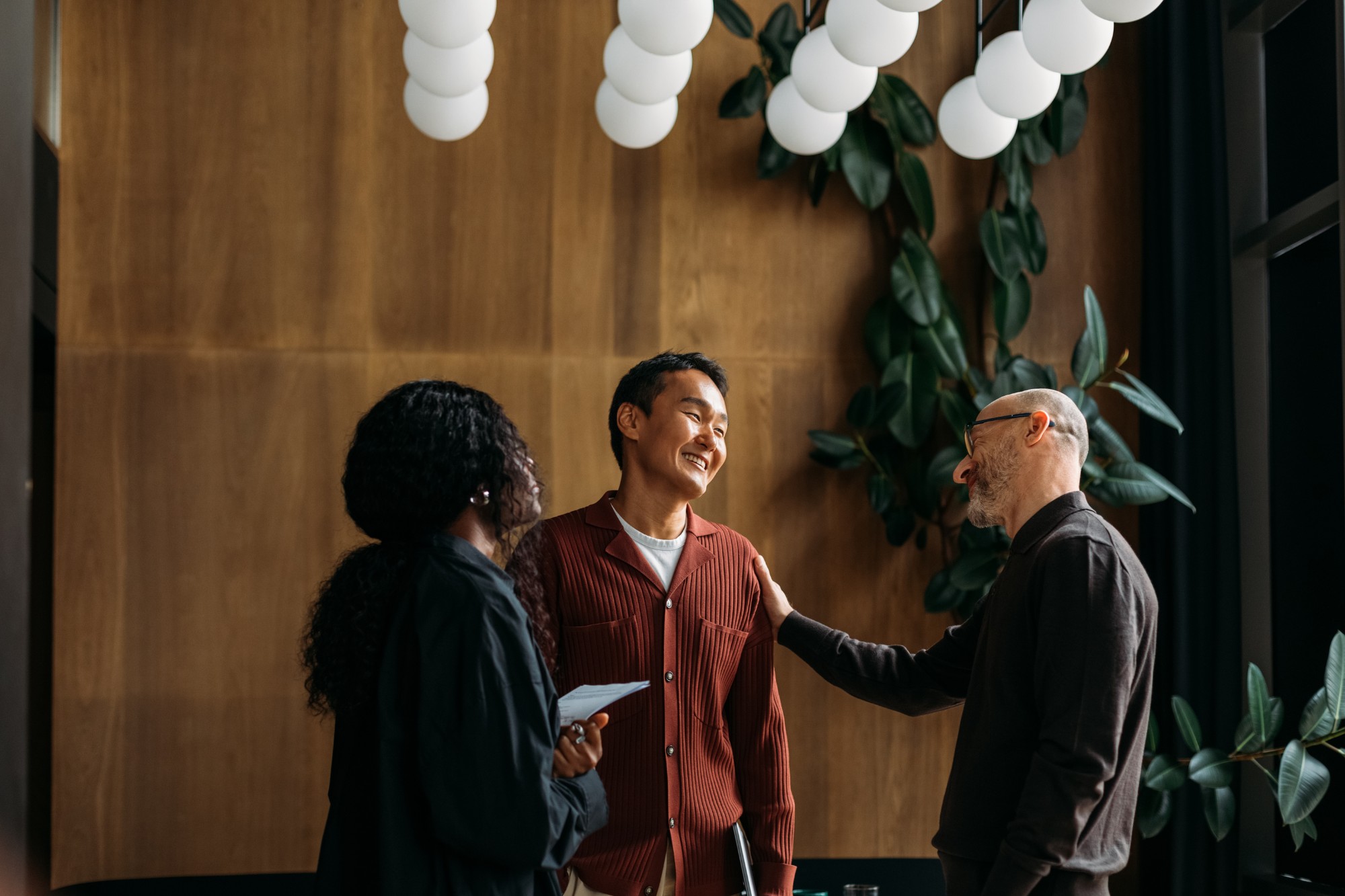 Three people talking and laughing together in a warm, plant-filled office